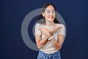 Young hispanic woman standing over blue background pointing to both sides with fingers, different direction disagree