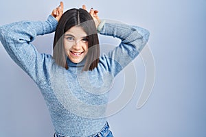 Young hispanic woman standing over blue background posing funny and crazy with fingers on head as bunny ears, smiling cheerful