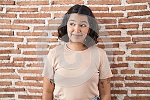 Young hispanic woman standing over bricks wall smiling looking to the side and staring away thinking