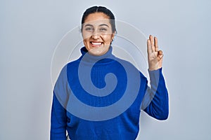 Young hispanic woman standing over isolated background showing and pointing up with fingers number three while smiling confident