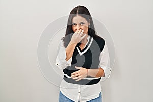 Young hispanic woman standing over isolated background smelling something stinky and disgusting, intolerable smell, holding breath