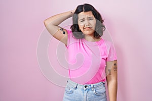 Young hispanic woman standing over pink background confuse and wondering about question