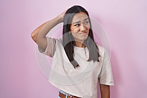 Young hispanic woman standing over pink background confuse and wondering about question