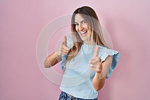 Young hispanic woman standing over pink background pointing fingers to camera with happy and funny face