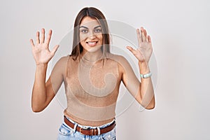 Young hispanic woman standing over white background showing and pointing up with fingers number ten while smiling confident and