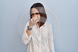 Young hispanic woman standing over white background smelling something stinky and disgusting, intolerable smell, holding breath