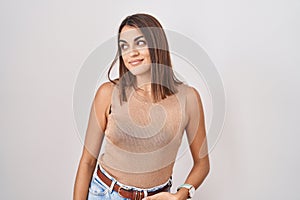 Young hispanic woman standing over white background smiling looking to the side and staring away thinking