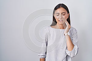 Young hispanic woman standing over white background touching mouth with hand with painful expression because of toothache or