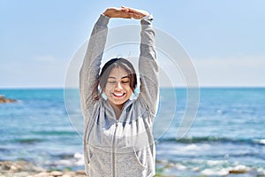 Young hispanic woman stretching arms training at seaside