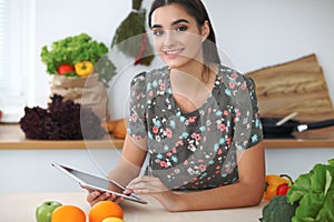 Young hispanic woman or student cooking in kitchen. Girl using tablet to make online shopping or find a new recipe.