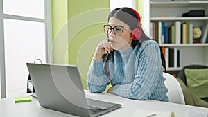 Young hispanic woman student using laptop studying wearing headphones at library university