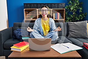 Young hispanic woman studying using computer laptop and headphones sticking tongue out happy with funny expression