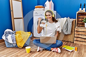 Young hispanic woman studying while waiting for laundry very happy and excited doing winner gesture with arms raised, smiling and