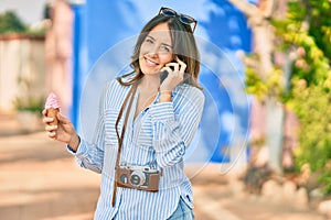Young hispanic woman talking on the smartphone and eating ice cream at the city