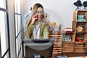 Young hispanic woman talking on the smartphone working at clothing store