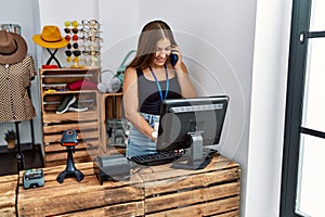 Young hispanic woman talking on the smartphone working at clothing store