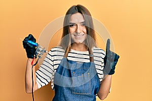 Young hispanic woman tattoo artist wearing professional uniform and gloves smiling with an idea or question pointing finger with