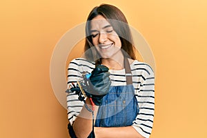 Young hispanic woman tattoo artist wearing professional uniform and gloves smiling and laughing hard out loud because funny crazy