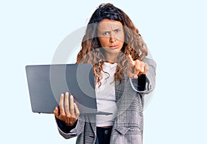 Young hispanic woman with tattoo holding laptop pointing with finger to the camera and to you, confident gesture looking serious