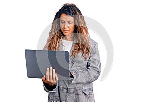 Young hispanic woman with tattoo holding laptop thinking attitude and sober expression looking self confident