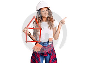 Young hispanic woman with tattoo wearing architect hardhat holding build project smiling happy pointing with hand and finger to