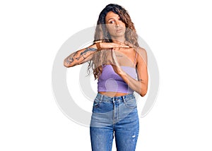 Young hispanic woman with tattoo wearing casual clothes doing time out gesture with hands, frustrated and serious face