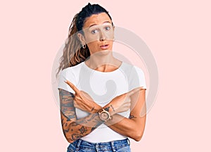 Young hispanic woman with tattoo wearing casual white tshirt pointing to both sides with fingers, different direction disagree