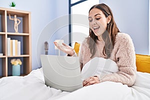 Young hispanic woman using computer laptop on the bed celebrating achievement with happy smile and winner expression with raised