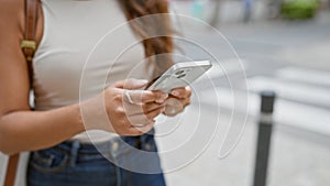 Young hispanic woman using her hands to text a message on her phone outdoors in the heart of the city street, connecting herself