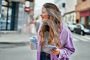 Young hispanic woman using smartphone drinking coffee at the city