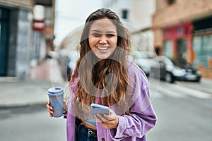 Young hispanic woman using smartphone drinking coffee at the city