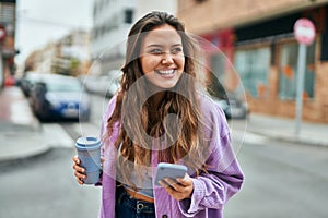 Young hispanic woman using smartphone drinking coffee at the city