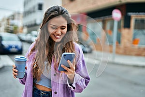 Young hispanic woman using smartphone drinking coffee at the city