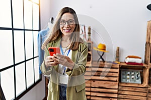 Young hispanic woman using smartphone working at clothing store