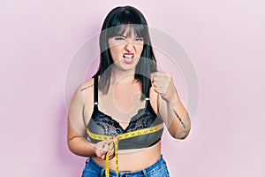 Young hispanic woman using tape measure measuring breast annoyed and frustrated shouting with anger, yelling crazy with anger and