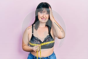 Young hispanic woman using tape measure measuring breast stressed and frustrated with hand on head, surprised and angry face
