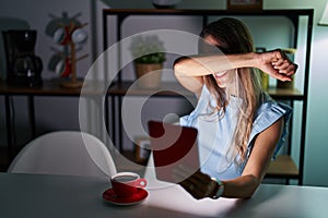 Young hispanic woman using touchpad sitting on the table at night smiling cheerful playing peek a boo with hands showing face