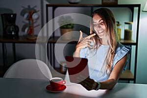 Young hispanic woman using touchpad sitting on the table at night smiling cheerful showing and pointing with fingers teeth and