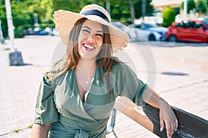 Young hispanic woman on vacation smiling happy sitting on bench at street of city