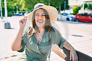 Young hispanic woman on vacation smiling happy sitting on bench at street of city