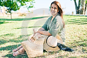 Young hispanic woman on vacation smiling happy sitting on the grass at park