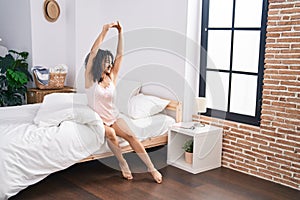 Young hispanic woman waking up stretching arms at bedroom