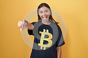 Young hispanic woman wearing bitcoin t shirt pointing to you and the camera with fingers, smiling positive and cheerful