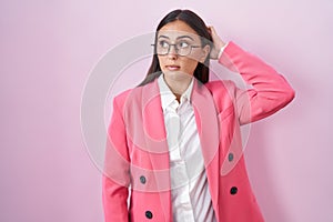 Young hispanic woman wearing business clothes and glasses confuse and wondering about question