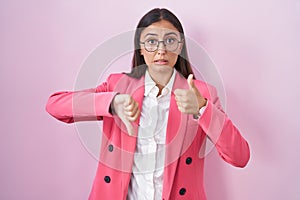 Young hispanic woman wearing business clothes and glasses doing thumbs up and down, disagreement and agreement expression