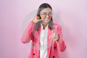 Young hispanic woman wearing business clothes and glasses smiling doing talking on the telephone gesture and pointing to you