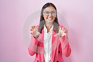 Young hispanic woman wearing business clothes and glasses smiling funny doing claw gesture as cat, aggressive and sexy expression