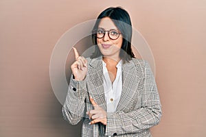 Young hispanic woman wearing business clothes and glasses smiling happy pointing with hand and finger to the side