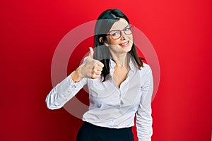 Young hispanic woman wearing business shirt and glasses doing happy thumbs up gesture with hand