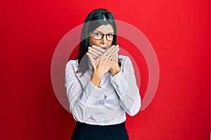Young hispanic woman wearing business shirt and glasses shocked covering mouth with hands for mistake